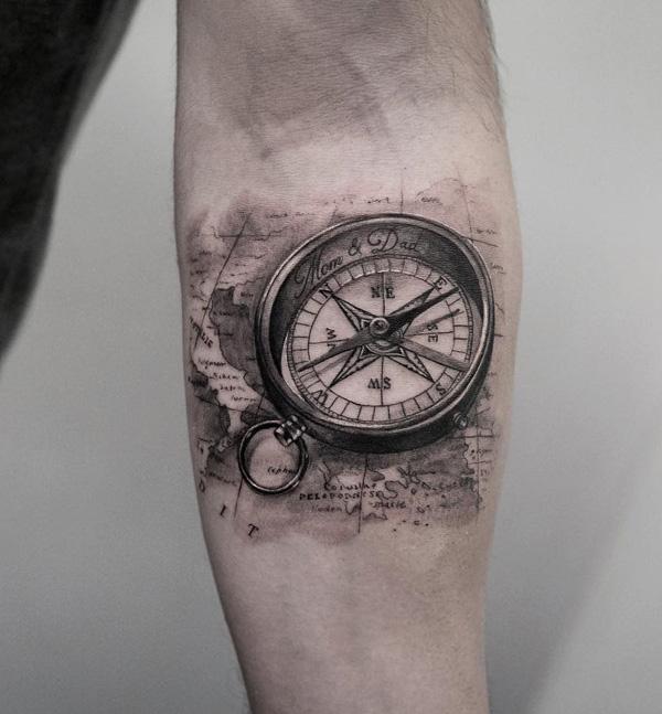 Musta ja harmaa pieni tatuointi kompassilla ja kartalla kyynärvarressa