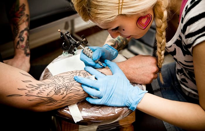 Lähikuva nuori nainen tekee tatuoinnin nuoren miehen käsivarteen.