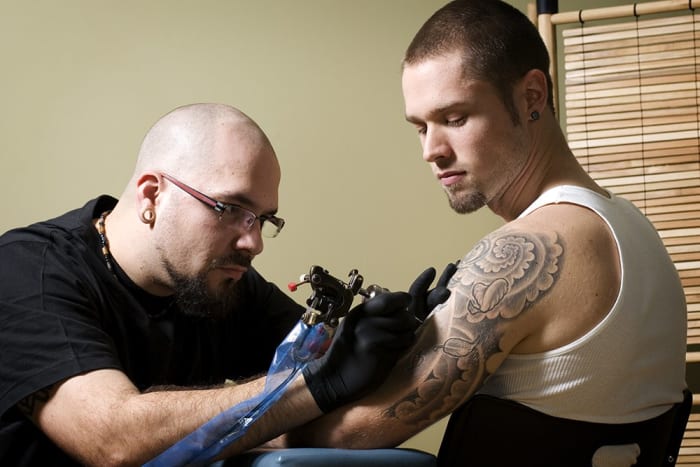 Tatuoija keskittyy antamaan jollekin tatuoinnin nuorelle miehelle