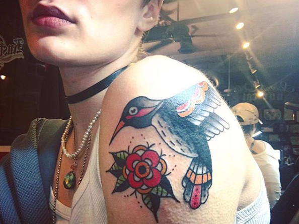 Στη συνέχεια, η Brendi K έχει ένα φωτεινό και τολμηρό παραδοσιακό κολιμπρί στον ώμο της. Το τατουάζ έκανε ο @cait.omen.