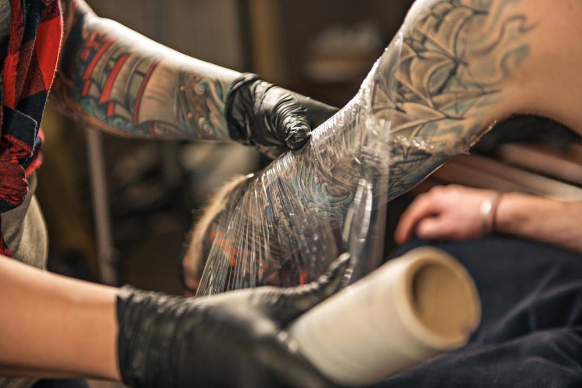 tatovering-kunstner-indpakning-klient-s-arm-i-plastik-film til at opmuntre-tatovering-healing