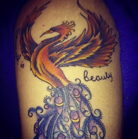 Her er hendes Phoenix/Peacock -tatovering placeret på hendes øverste venstre arm. Hun kombinerede dem for at vise sin styrke og elegance til verden og sig selv. Ved siden af ​​fuglen står der: