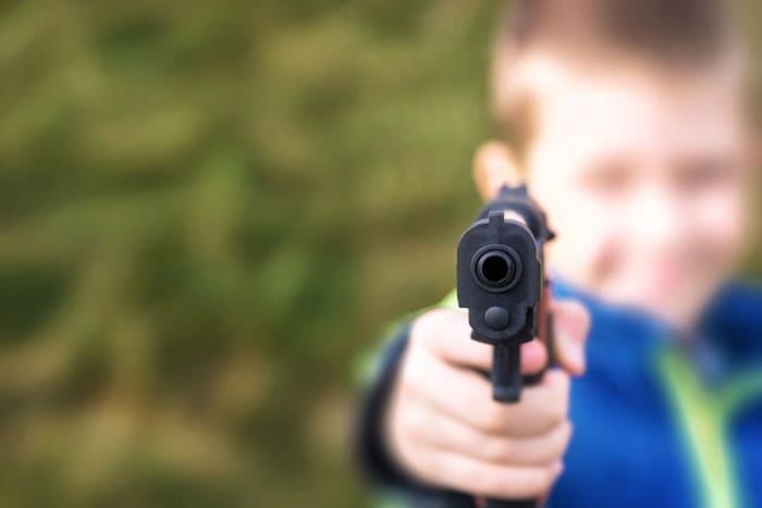 nuori poika osoittaa aseella kameraan